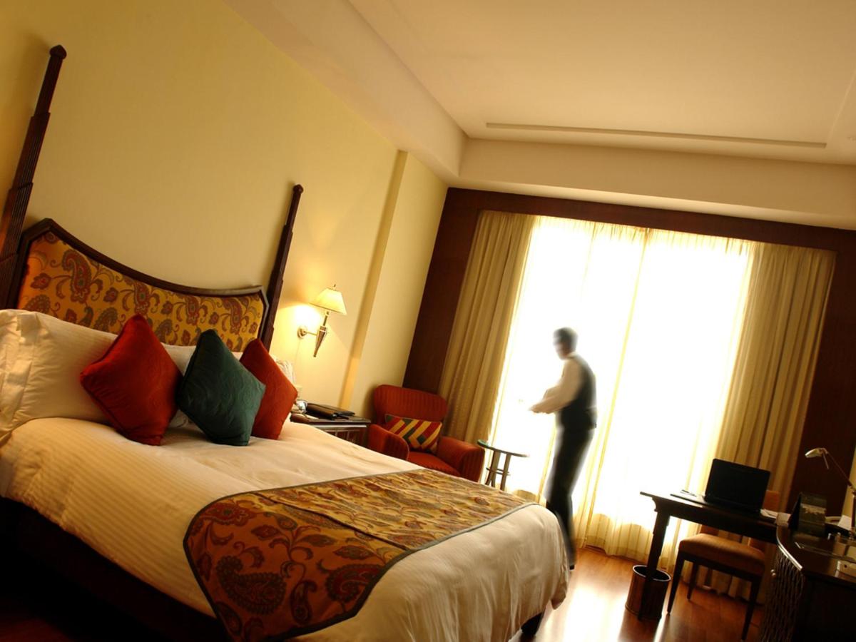 a hotel room with a bed and a man looking out the window at The Lalit Mumbai in Mumbai