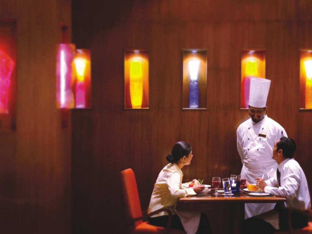 three people sitting at a table in a restaurant with a chef at The Lalit Mumbai in Mumbai