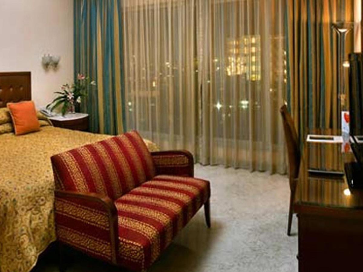 a bedroom with a bed and a chair and a window at The Lalit Mumbai in Mumbai