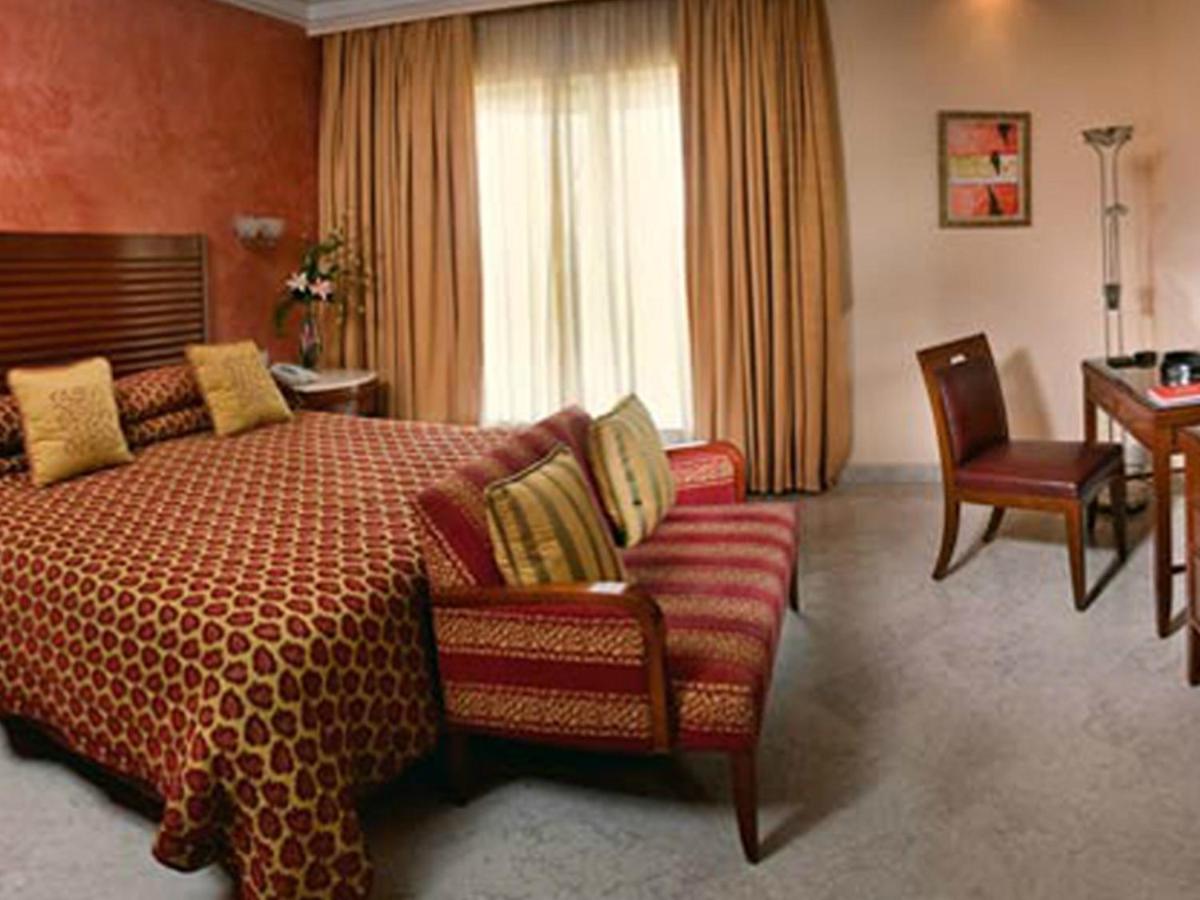 a bedroom with a bed and a chair and a desk at The Lalit Mumbai in Mumbai