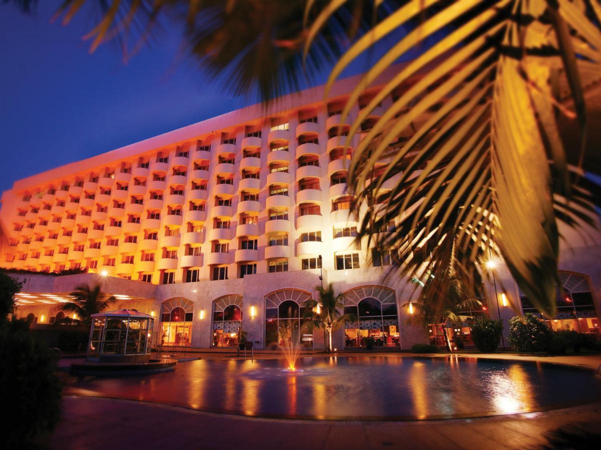 a hotel building with a palm tree in front of it at The Lalit Mumbai in Mumbai