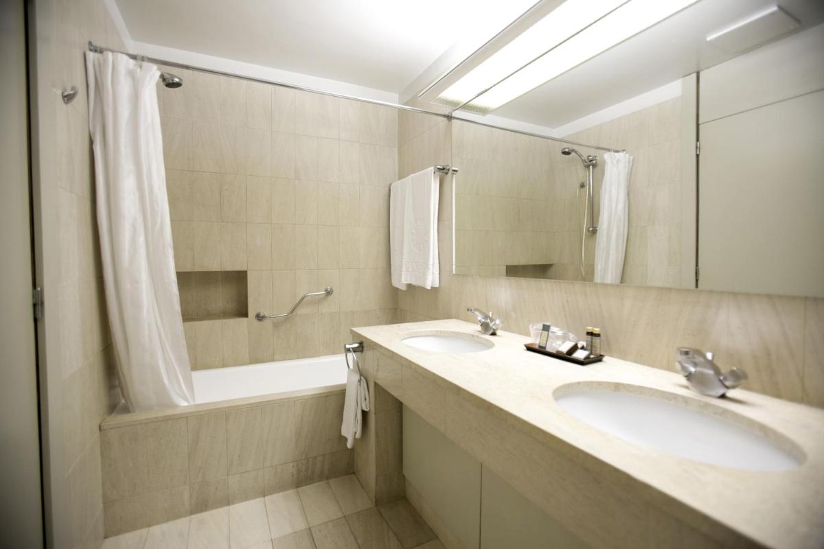 um banheiro com duas pias, um espelho e uma banheira em Hotel Solverde Spa and Wellness Center em Vila Nova de Gaia um banheiro com duas pias, um espelho e uma banheira em Hotel Solverde Spa and Wellness Center em Vila Nova de Gaia