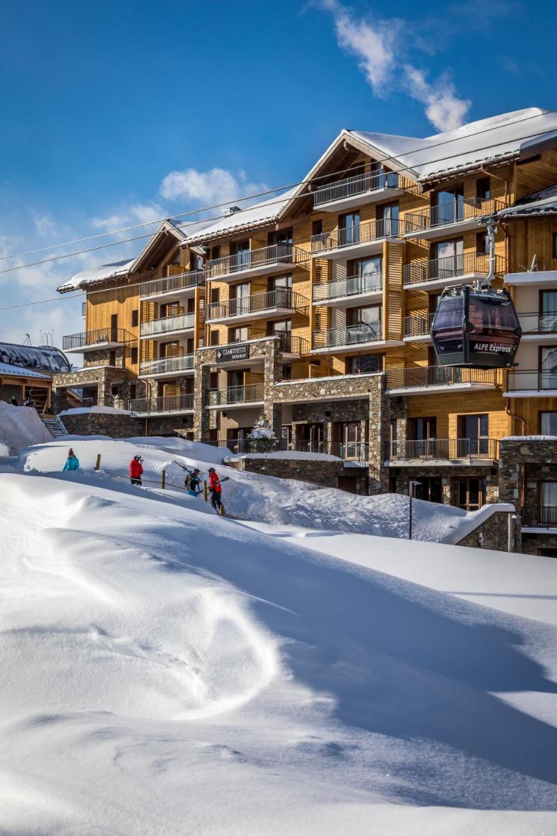 un groupe de personnes skier dans la neige devant un hôtel dans l'établissement Résidence Daria-I Nor by les Etincelles, à L'Alpe-d'Huez