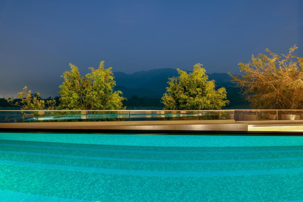 a swimming pool with trees and mountains in the background at Modi Yoga Retreat Rishikesh in Rishīkesh