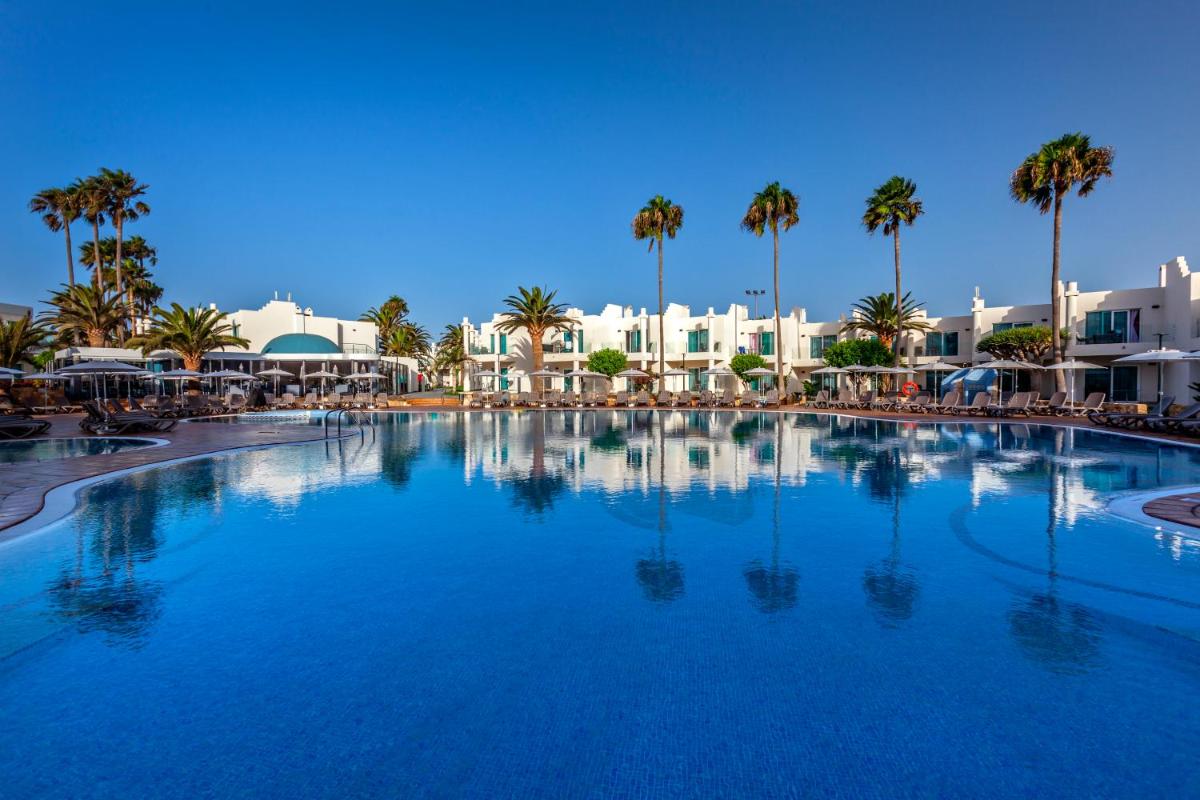 Una gran piscina con palmeras y edificios. en Barceló Corralejo Sands, en Corralejo