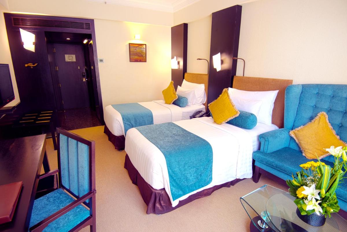 a hotel room with two beds and a blue chair at Sterlings Mac Hotel in Bengaluru