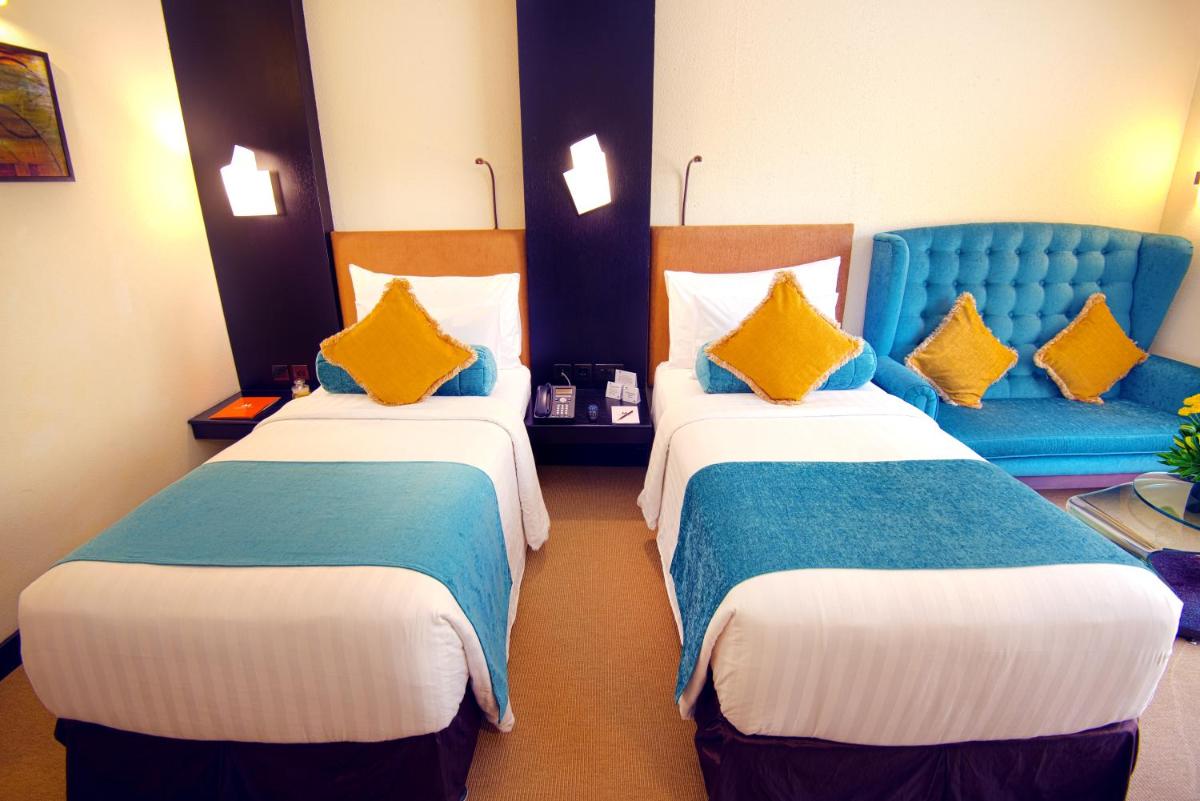 a hotel room with two beds and a blue chair at Sterlings Mac Hotel in Bengaluru