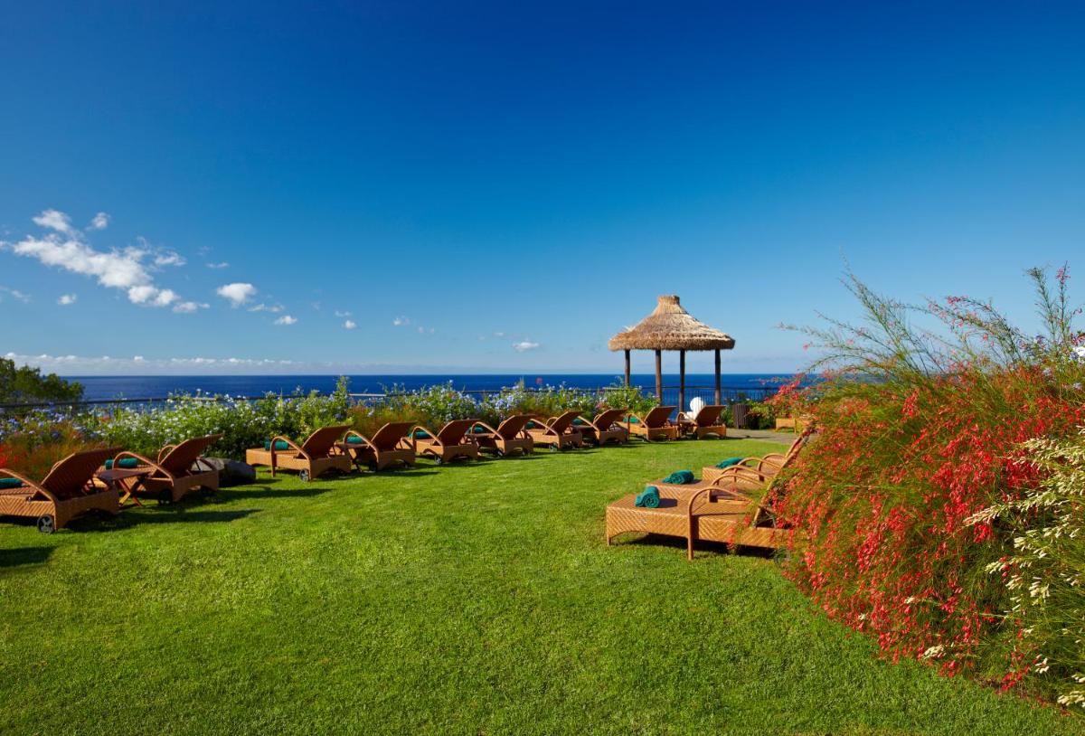 uma fila de bancos sentados na relva perto do oceano em The Residence Porto Mare - PortoBay no Funchal