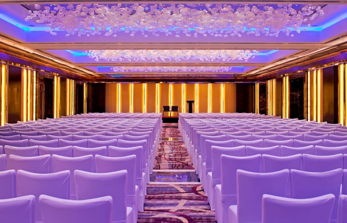 a row of white chairs in a room with a stage at Radisson Blu Plaza Delhi Airport in New Delhi a row of white chairs in a room with a stage at Radisson Blu Plaza Delhi Airport in New Delhi