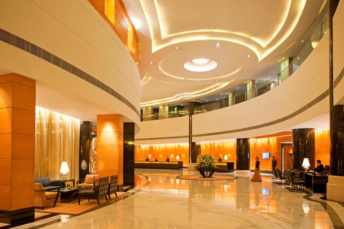 a lobby of a hotel with chairs and tables at Radisson Blu Plaza Delhi Airport in New Delhi a lobby of a hotel with chairs and tables at Radisson Blu Plaza Delhi Airport in New Delhi