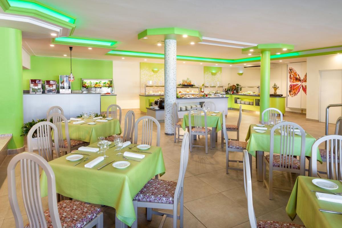 un restaurante con mesas verdes y sillas y una cocina en Hotel Tropical Park, en Callao Salvaje