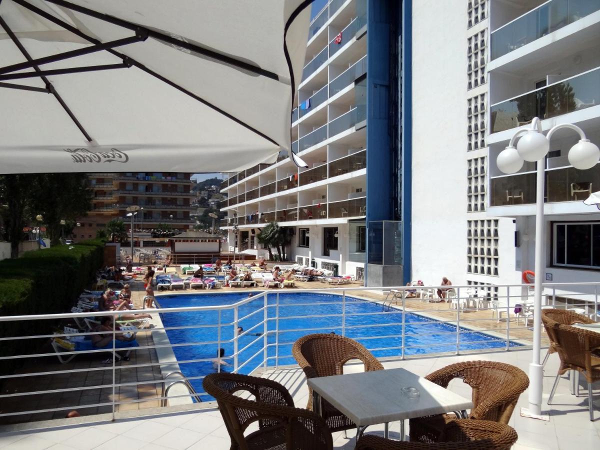 una piscina con sillas, una mesa y una sombrilla en Hotel Riviera, en Santa Susanna una piscina con sillas, una mesa y una sombrilla en Hotel Riviera, en Santa Susanna