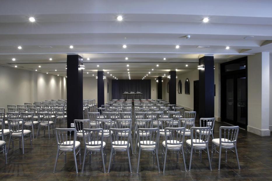 Una gran sala con filas de sillas y un escenario. en Hotel Palacio de Mengibar, en Mengíbar