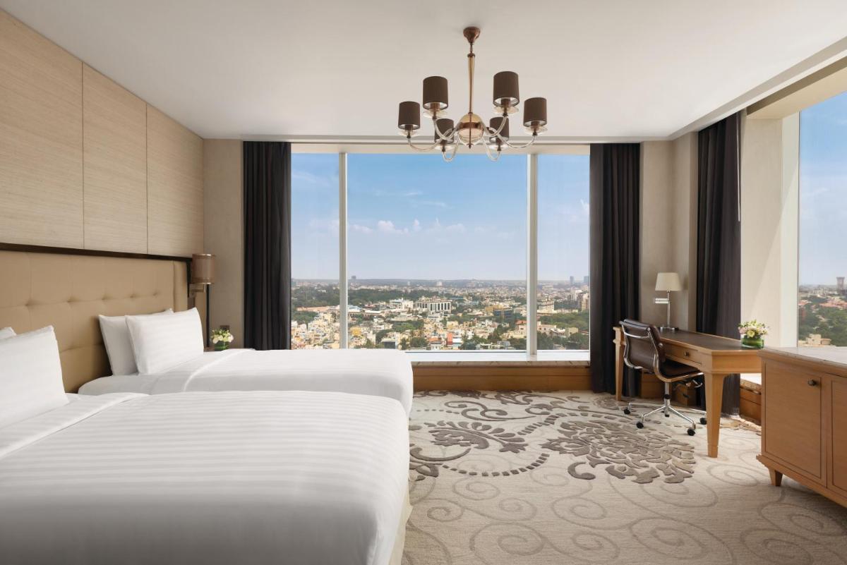 a hotel room with two beds and a desk and a window at Shangri-La Bengaluru in Bengaluru a hotel room with two beds and a desk and a window at Shangri-La Bengaluru in Bengaluru