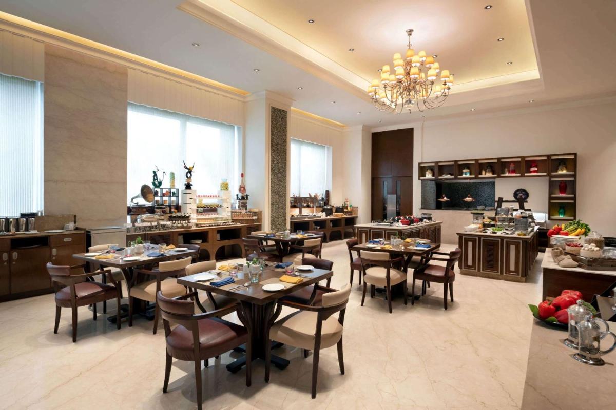 a dining room with tables and chairs and a kitchen at Ramada Plaza Chennai in Chennai