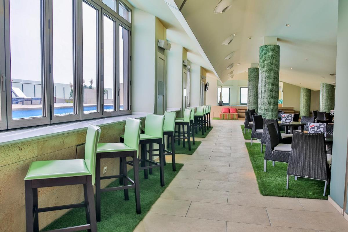 Un restaurante con sillas y mesas verdes y ventanas. en Hotel 525, en Los Alcázares