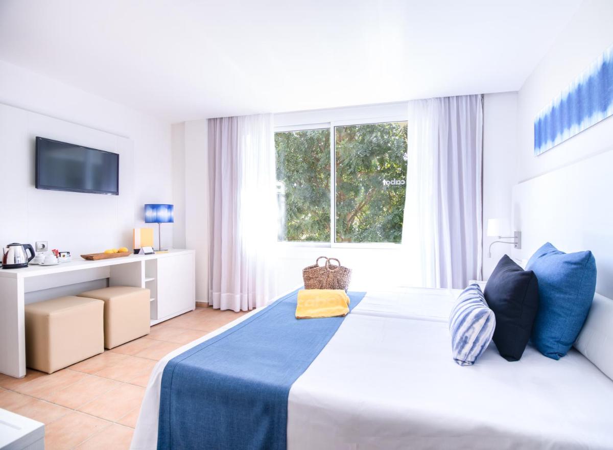 Un dormitorio con una cama con una manta azul y una ventana. en Cabot Pollensa Park Spa, en Puerto Pollensa