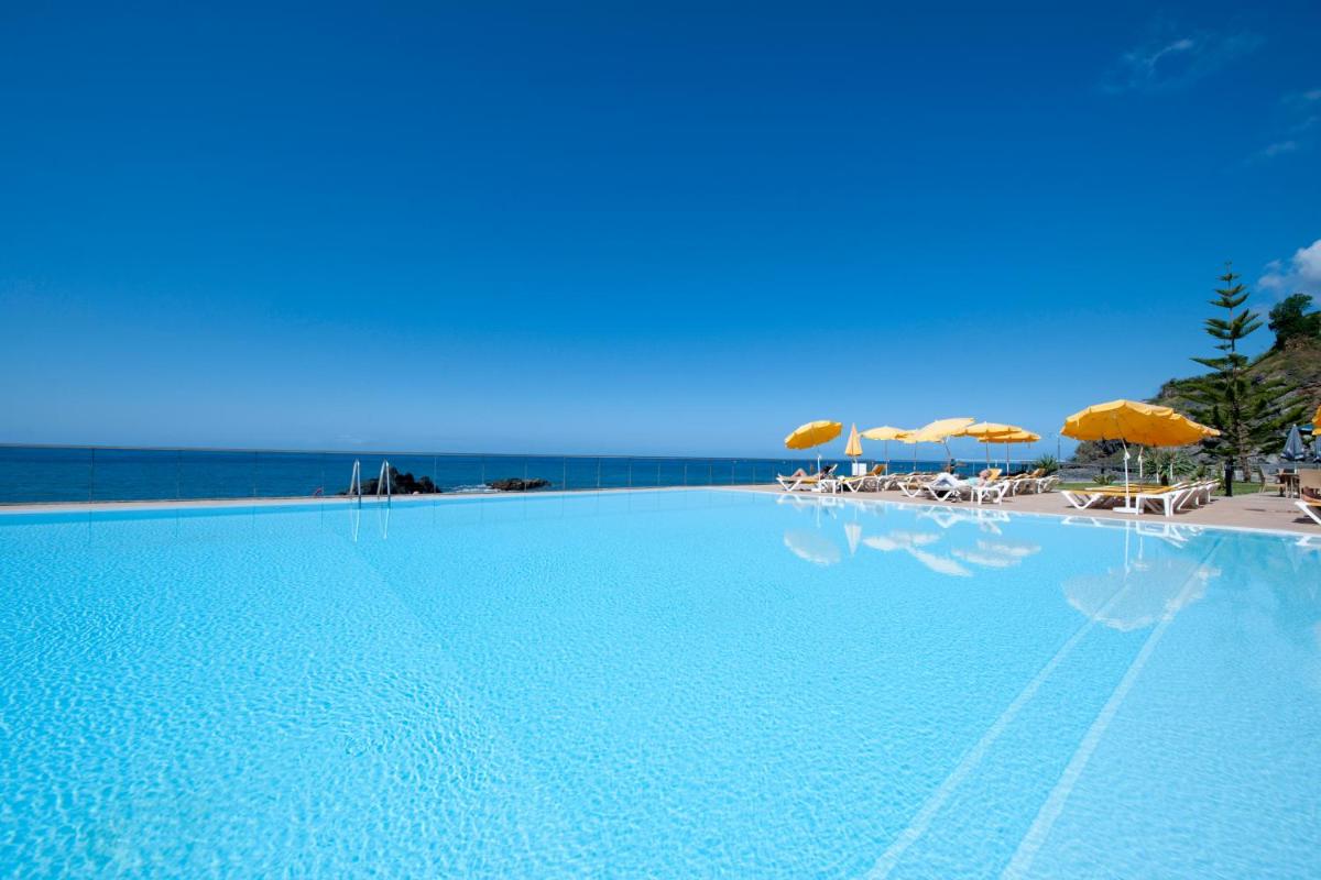 uma grande piscina com cadeiras e guarda-sóis em Hotel Orca Praia no Funchal mais 44 fotografias