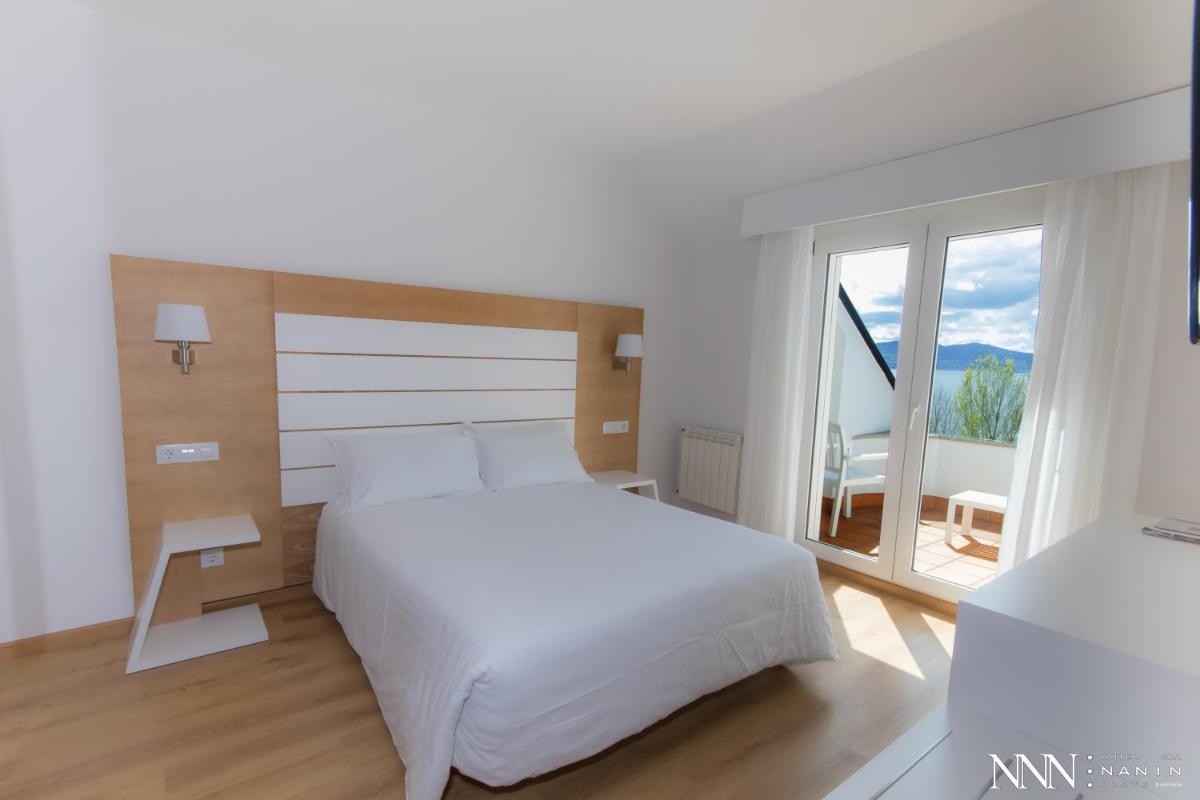 Un dormitorio con una cama blanca y una ventana grande. en Hotel Spa Nanin Playa, en Sanxenxo