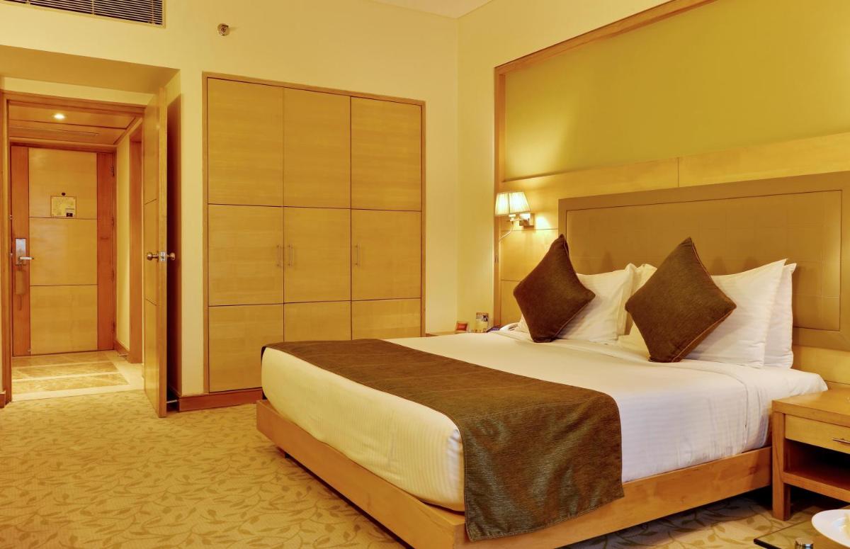 a hotel room with a large bed and a bathroom at The Suryaa New Delhi in New Delhi a hotel room with a large bed and a bathroom at The Suryaa New Delhi in New Delhi