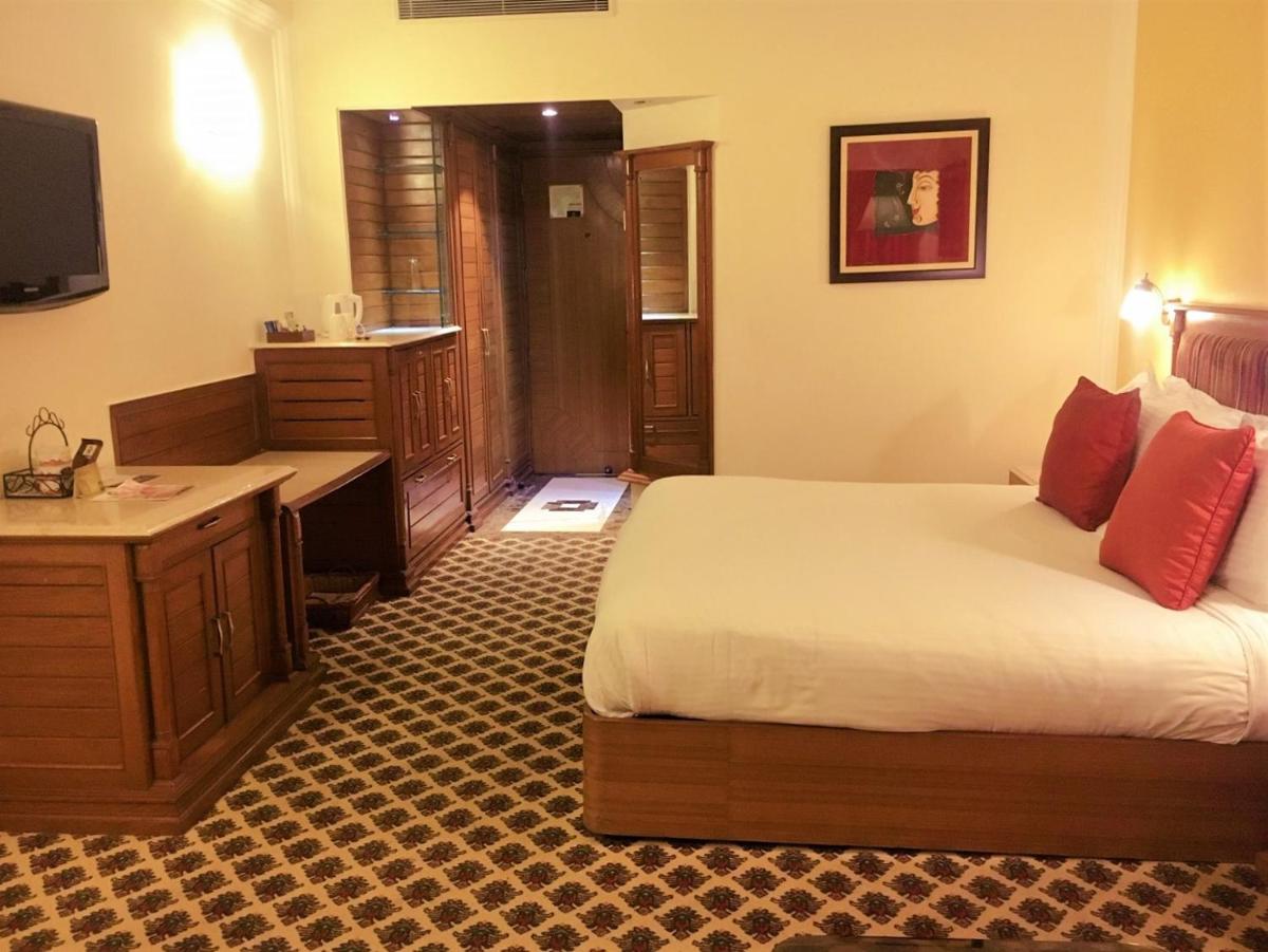 a hotel room with a bed and a desk and a desk at The Suryaa New Delhi in New Delhi a hotel room with a bed and a desk and a desk at The Suryaa New Delhi in New Delhi