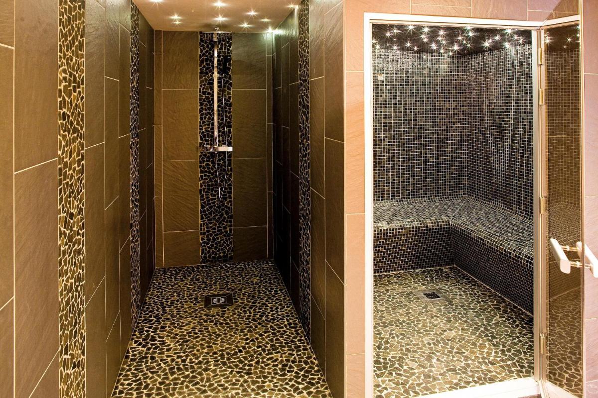 une salle de bain avec une douche avec une porte vitrée dans l'établissement Hôtel Belalp, à Châtel