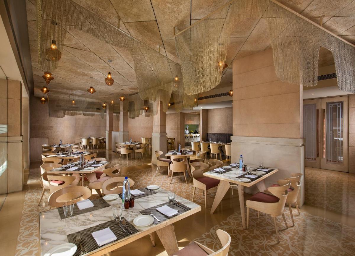 a restaurant with tables and chairs in a room at Sarovar Premiere Jaipur in Jaipur