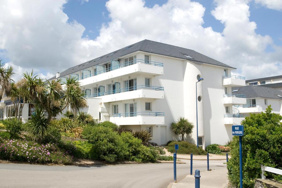 un bâtiment blanc avec des palmiers devant dans l'établissement Résidence Pierre & Vacances la Corniche de la Plage, à Bénodet