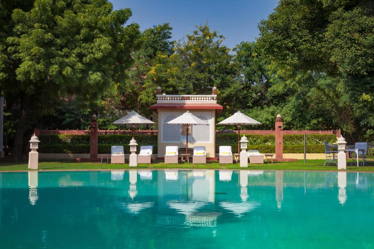 a swimming pool with chairs and umbrellas in a park at Jai Mahal Palace in Jaipur