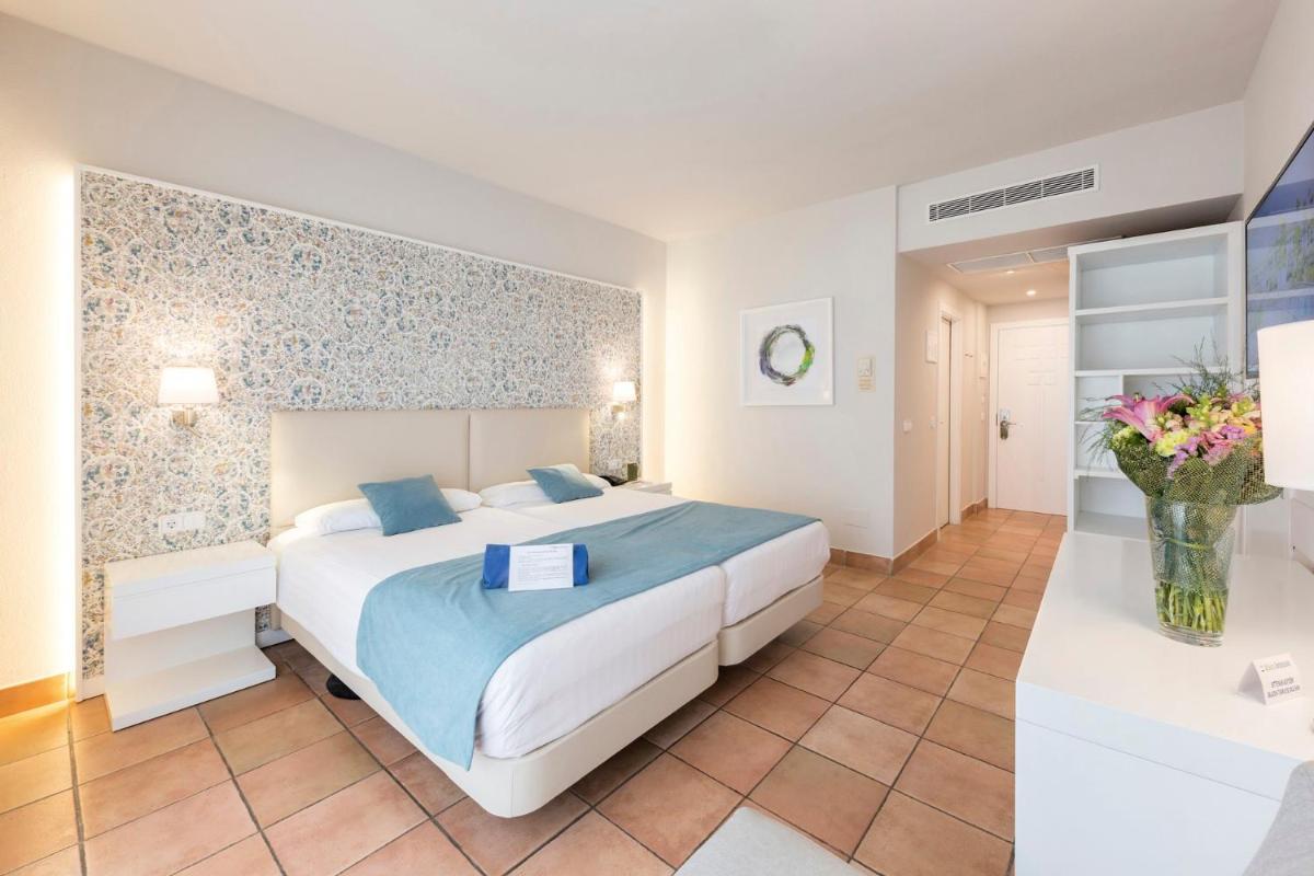 Un dormitorio con una cama grande y un jarrón de flores. en Aldiana Club Andalusien, en Chiclana de la Frontera