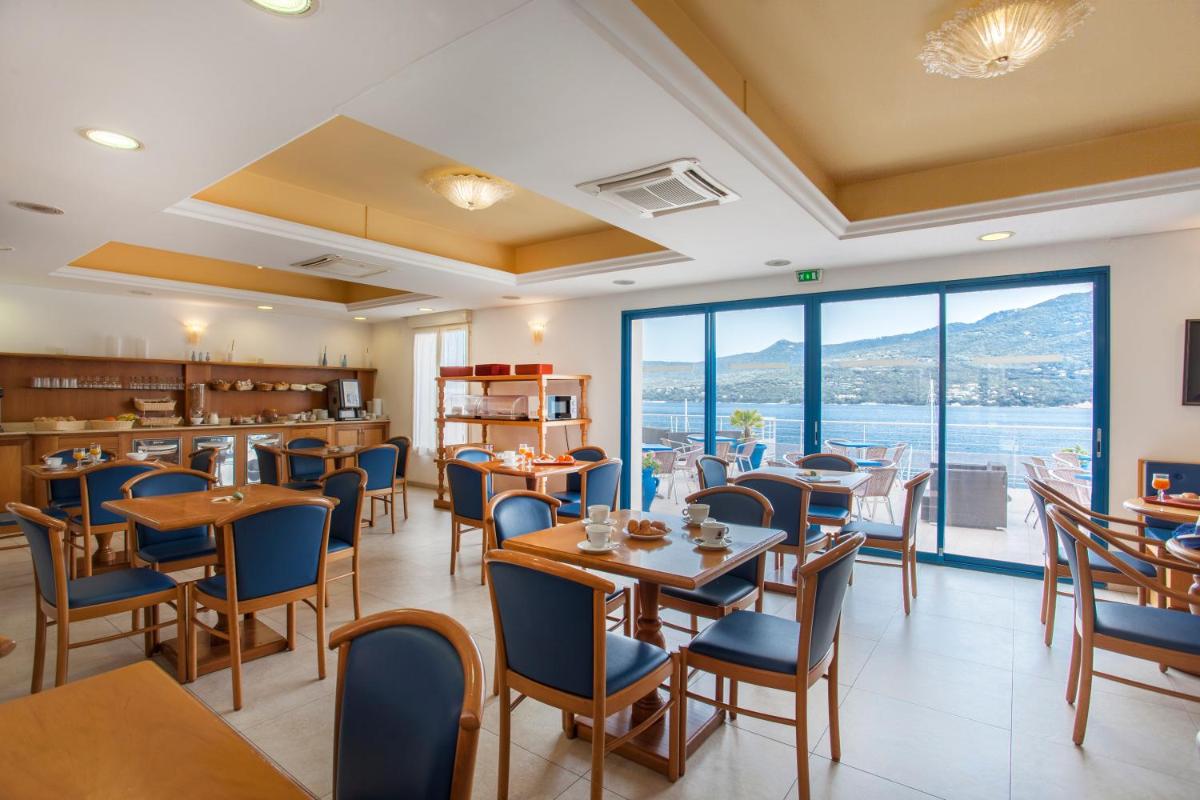 un restaurant avec des tables et des chaises et une grande fenêtre dans l'établissement Le Neptune & Spa, à Propriano