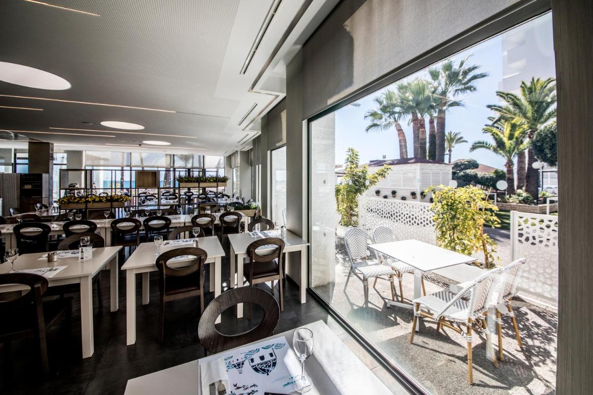Un restaurante con mesas y sillas y un gran ventanal. en Hotel Cap Negret, en Altea