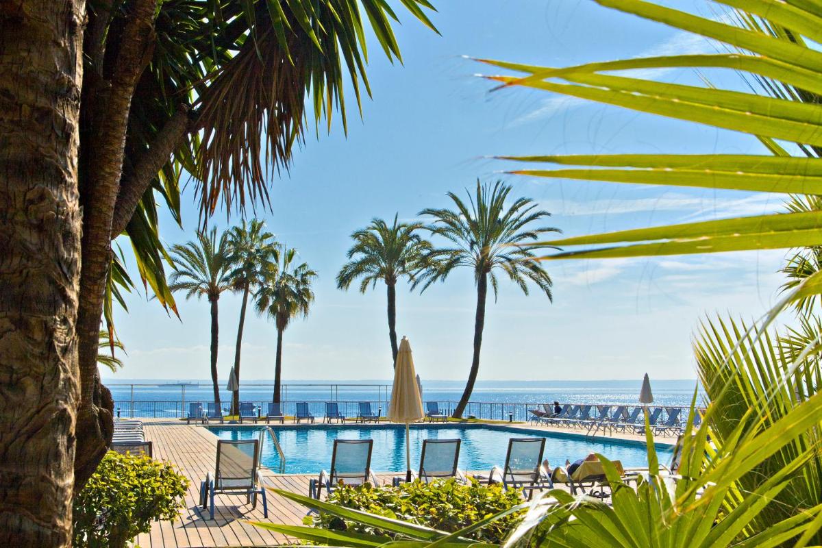 Una piscina con sillas y palmeras y el océano. en Palace Bonanza Playa Resort & SPA by Olivia Hotels Collection, en Illetas