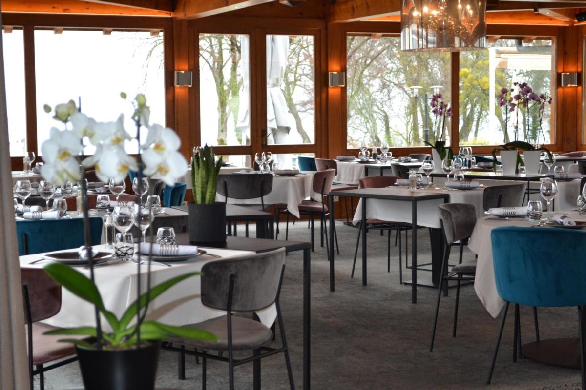 un restaurant avec des tables et des chaises blanches et des fenêtres dans l'établissement Le Pré de la Cure, à Yvoire