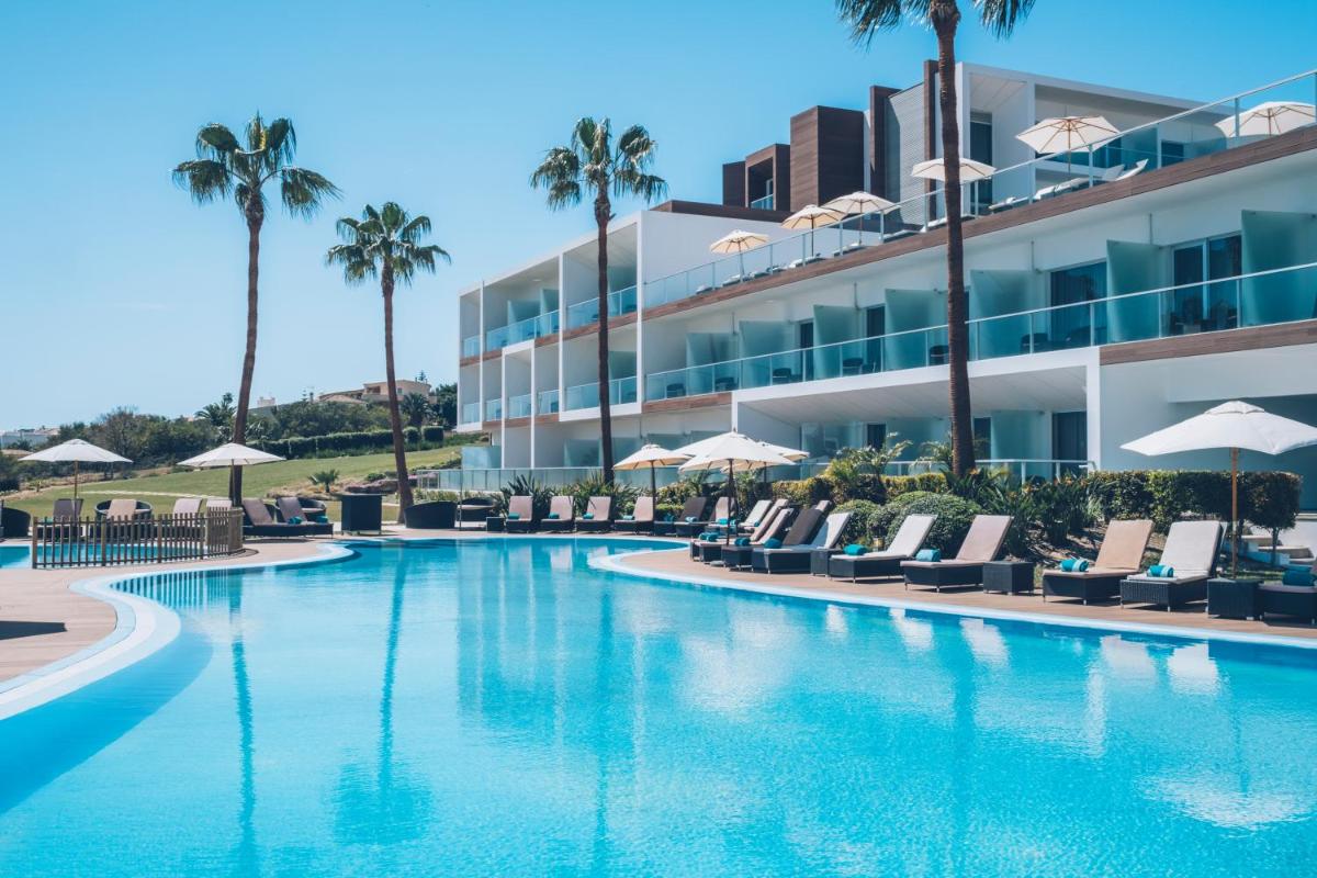 uma piscina com cadeiras e palmeiras em frente a um edifício em Iberostar Selection Lagos Algarve em Lagos