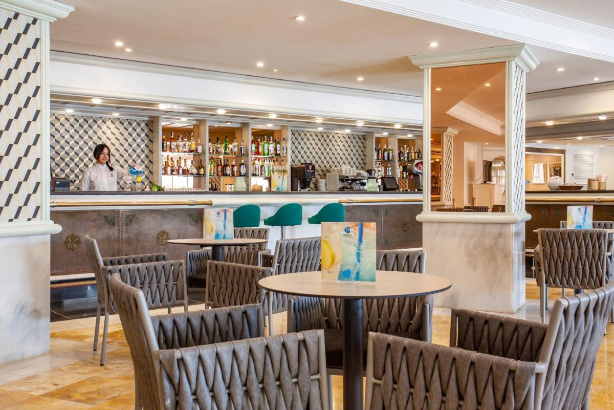 Un restaurante con mesas y sillas frente a un mostrador. en Grupotel Los Príncipes & Spa, en Playa de Muro
