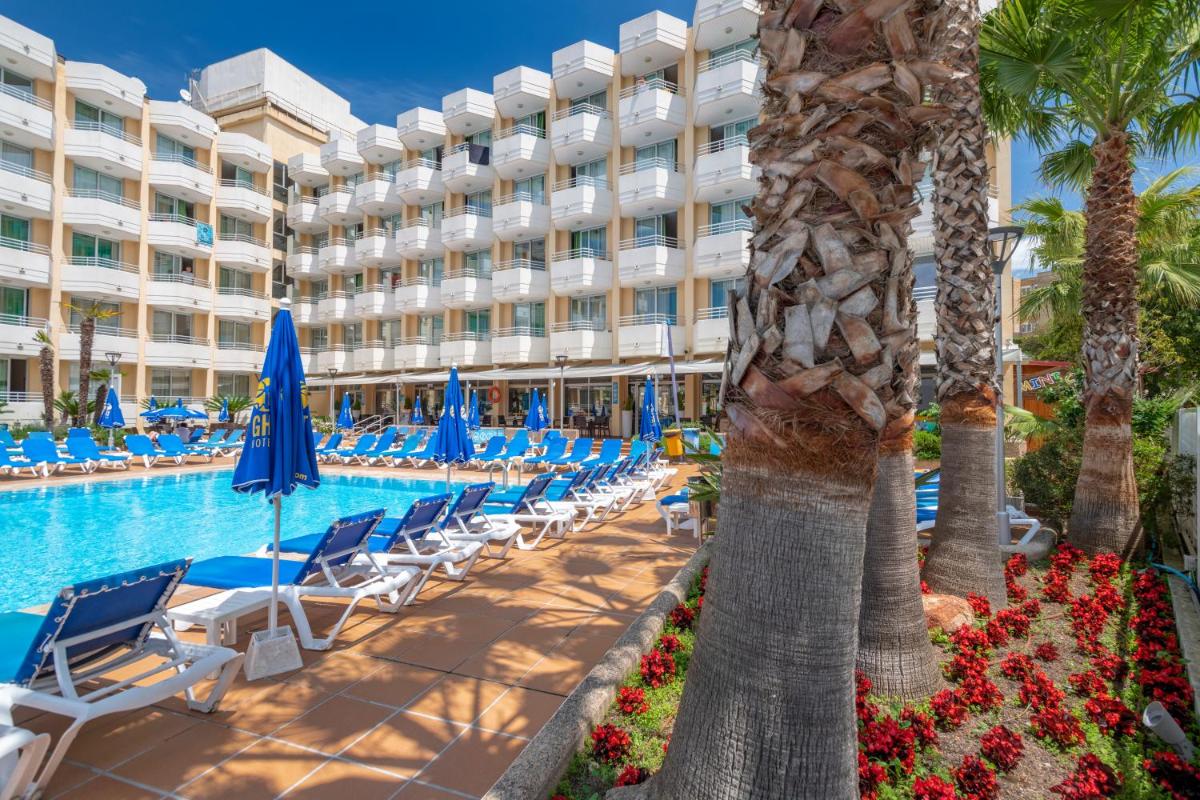un hotel con sillas, piscina y palmeras en GHT Oasis Tossa & Spa, en Tossa de Mar