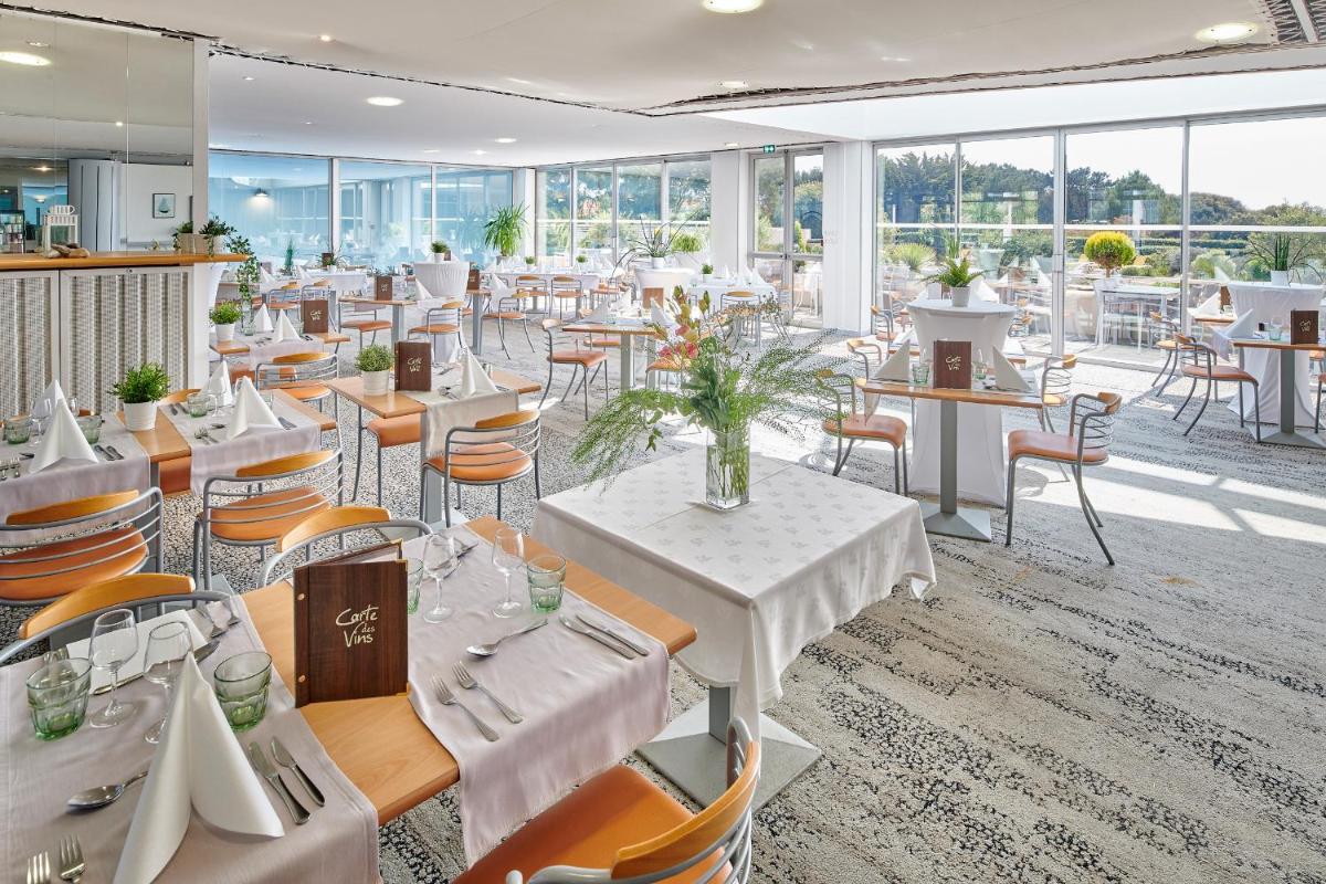 un restaurant avec des tables et des chaises blanches et des fenêtres dans l'établissement Club Vacances Bleues Les Jardins De l'Atlantique, à Talmont-Saint-Hilaire
