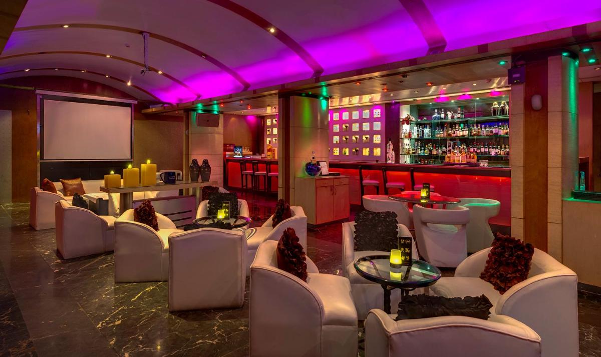 a restaurant with white chairs and a bar with purple lighting at Hotel Hindusthan International, Kolkata in Kolkata