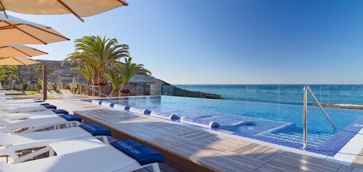 Una piscina con tumbonas y vista al mar. en H10 Costa Adeje Palace, en Adeje