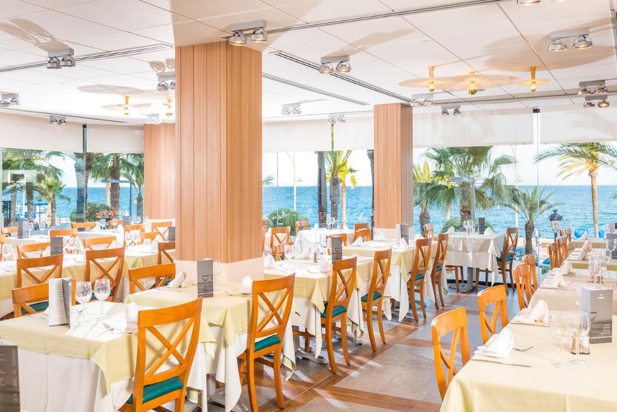 Un restaurante con mesas y sillas con el océano de fondo. en Hotel Marsol, en Lloret de Mar