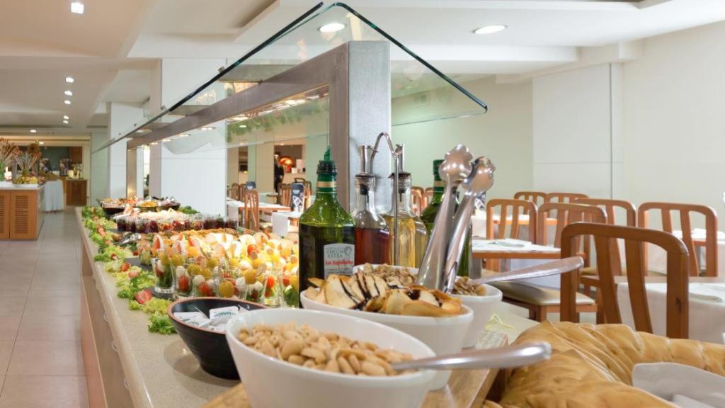 una línea de buffet con tazones de comida y botellas de vino en Hotel Riviera, en Santa Susanna