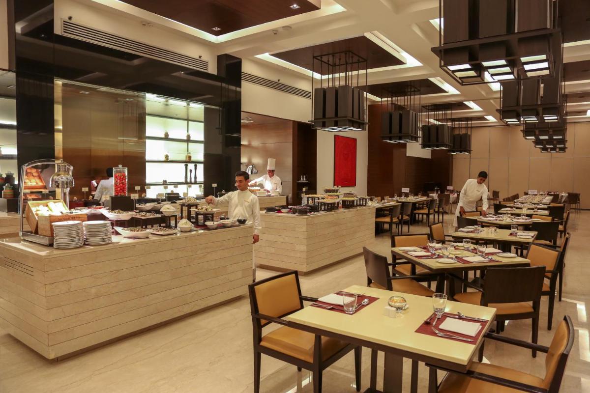a restaurant with tables and a chef preparing food at Trident Agra in Agra
