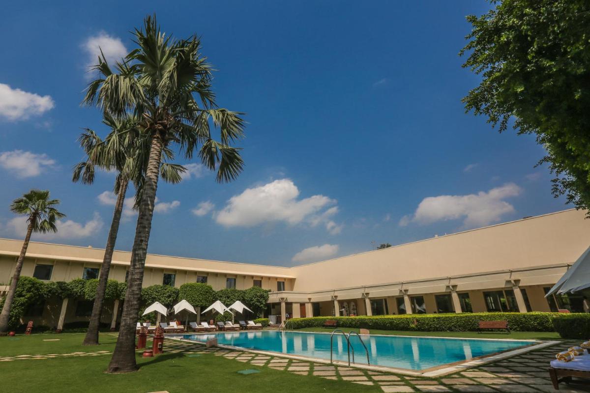 a large building with a swimming pool and palm trees at Trident Agra in Agra