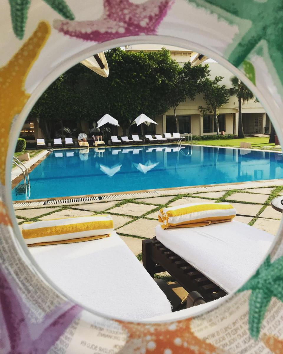 a mirror reflection of a swimming pool with chaise lounge chairs at Trident Agra in Agra