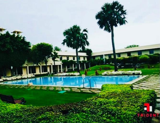 a swimming pool in front of a building with palm trees at Trident Agra in Agra