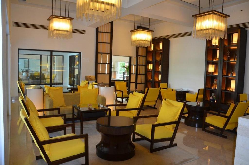 a room with yellow chairs and tables and chandeliers at Trident Agra in Agra