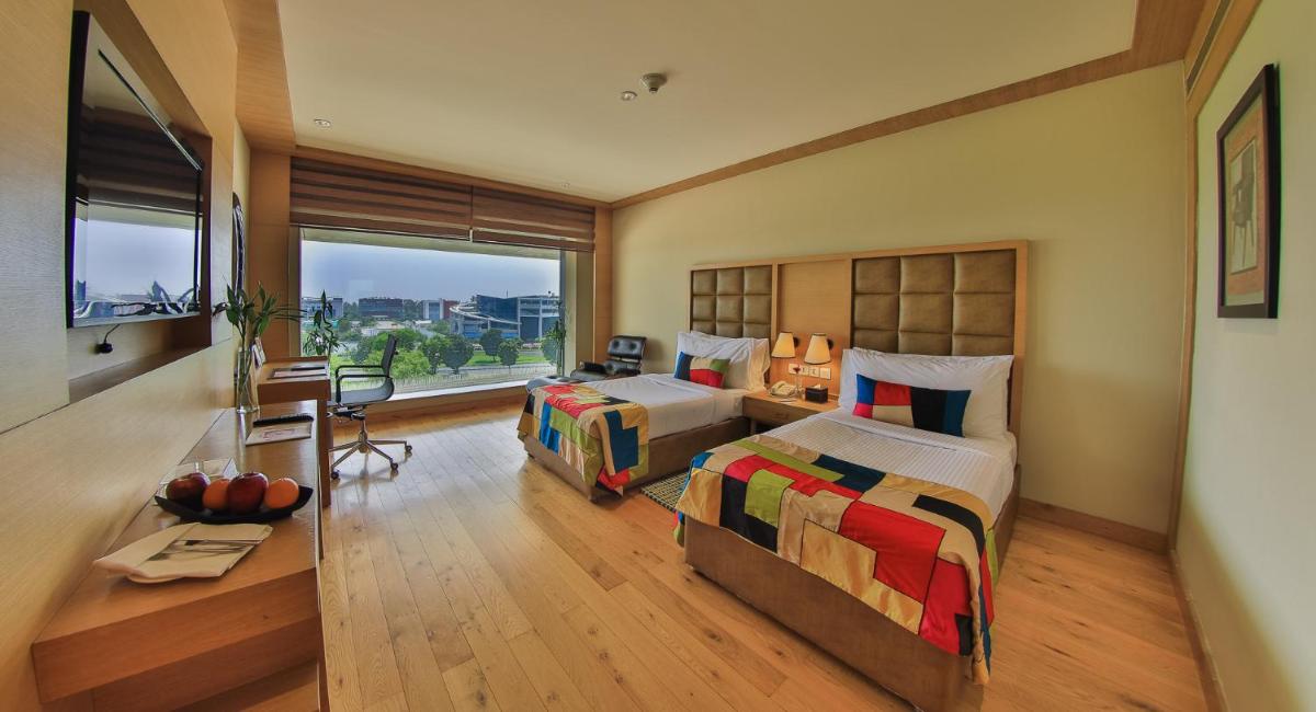 a bedroom with two beds and a desk and a window at The Lalit Chandigarh in Chandīgarh