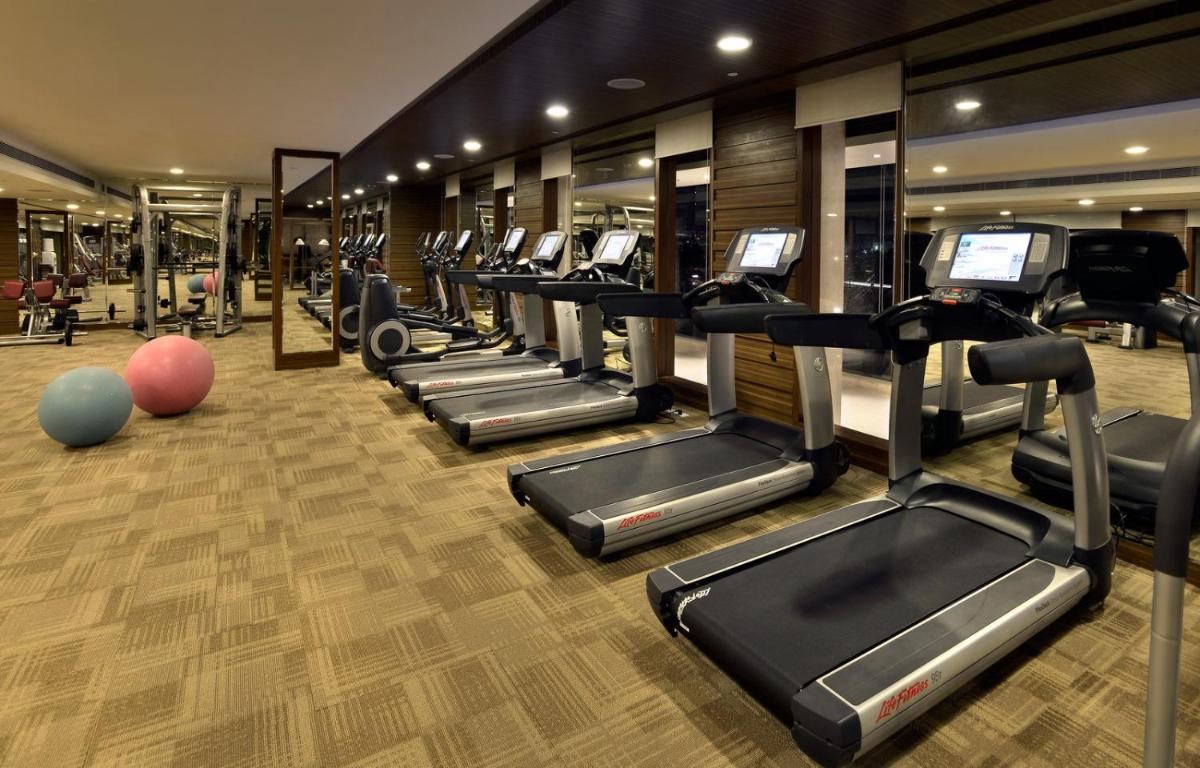 a gym with a row of treadmills and ellipticals at The Lalit Chandigarh in Chandīgarh