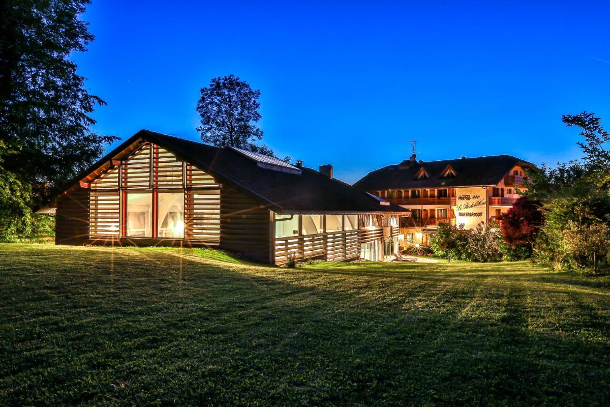 une maison en bois sur un champ en face d'un bâtiment dans l'établissement Le Pré de la Cure, à Yvoire